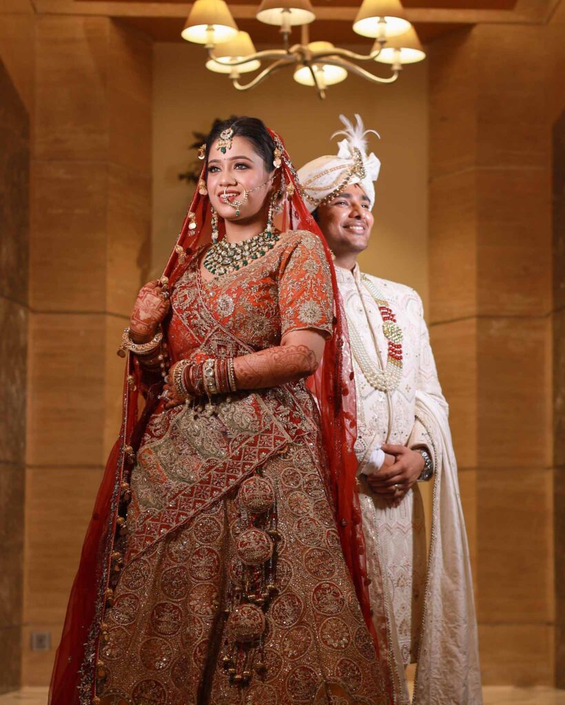 Full view of a bride in red lehnga and groom in white shervani