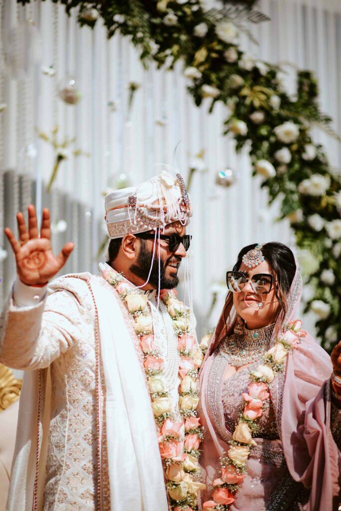 Smiling bride in pink lehnga and groom in cream shervani