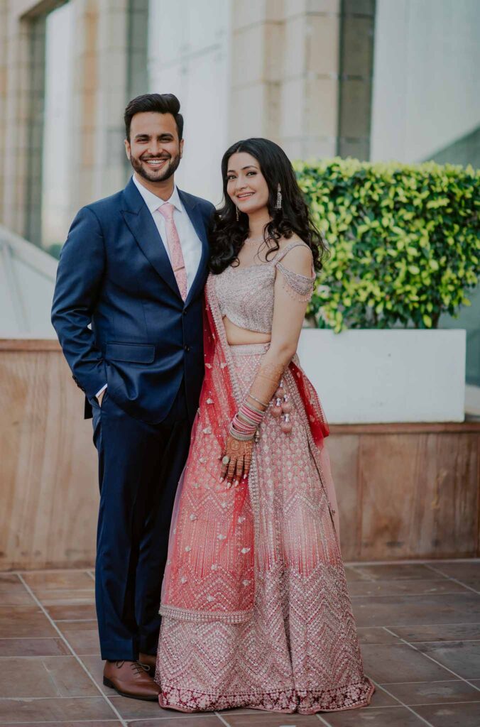 groom smiling in blue suit and bride in red lehnga
